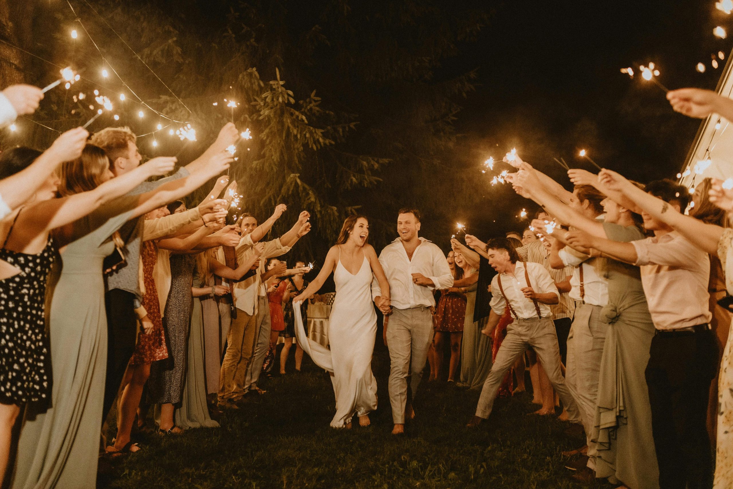 Newlyweds walking through guests holding sparklers at a night wedding